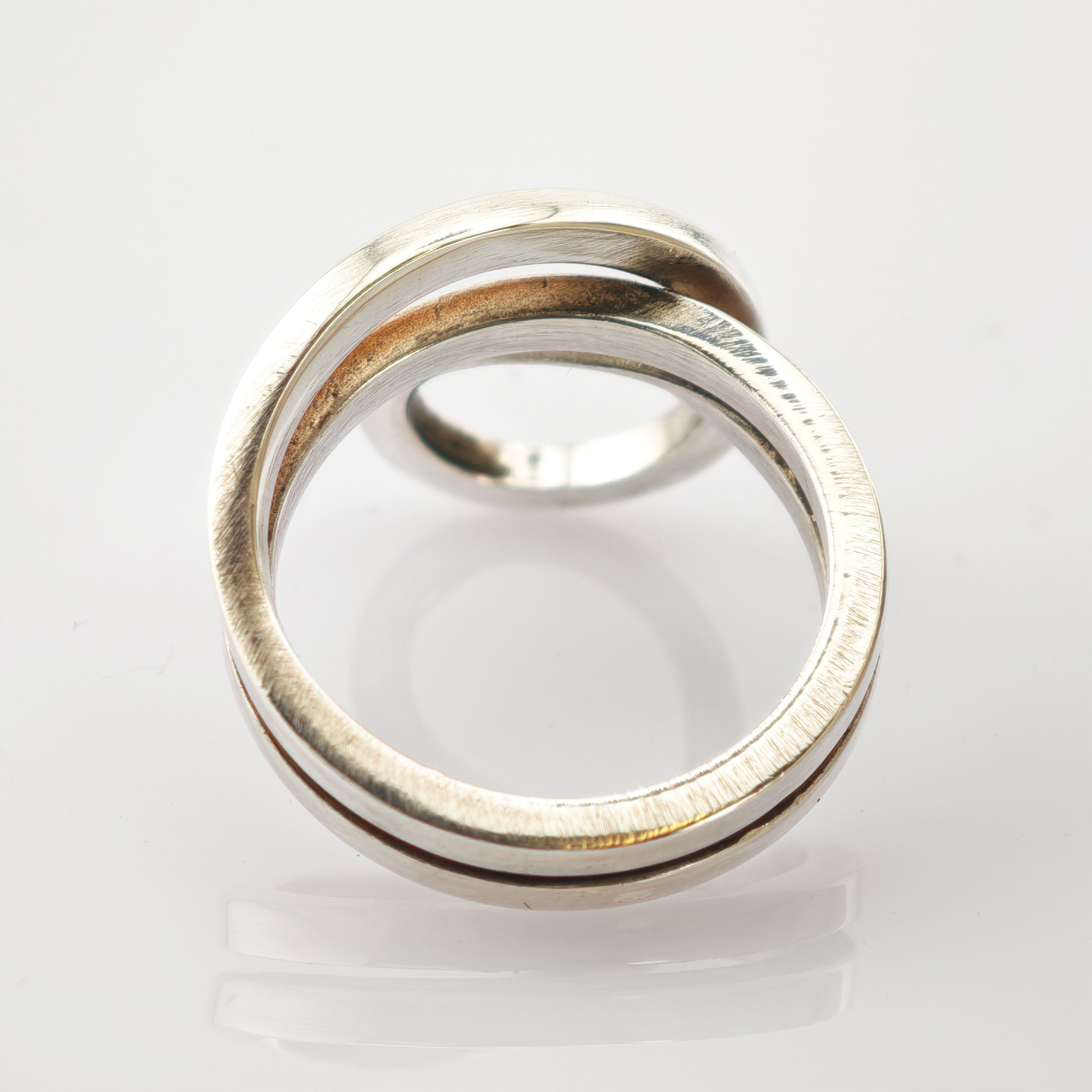 Zwei ineinander verschlungene Silberringe auf weißem reflektierendem Untergrund.