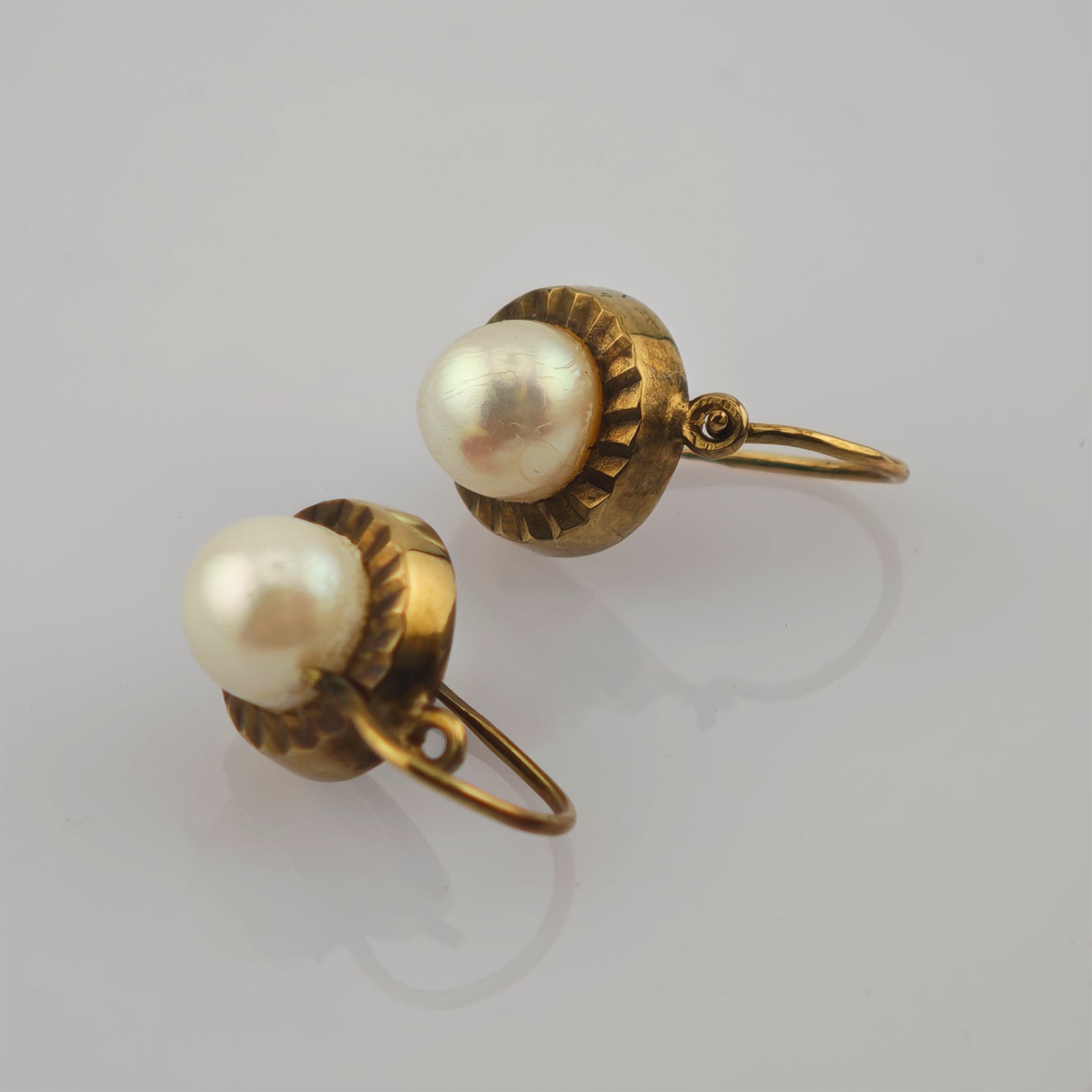 Vintage-Goldohrringe mit großen weißen Perlen in runder Fassung auf hellem Hintergrund