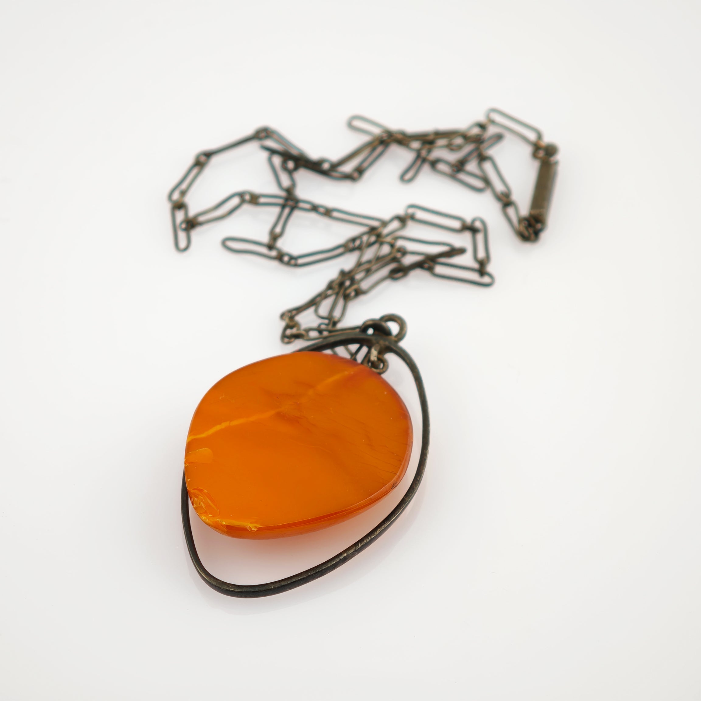 Vintage Halskette mit orangefarbenem poliertem Edelstein in unregelmäßigem Metallrahmen an dunkler Metallkette.