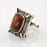 Rechteckiger Vintage-Ring mit poliertem braunem Bernstein und silbernem Rahmen mit Wirbelmustern.