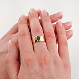 Zwei weibliche Hände mit gepflegten Nägeln und einem Goldring mit schwarzem ovalem Edelstein am rechten Ringfinger