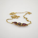 Zarte Goldkette mit Armband und zentraler Leiste aus drei dunkelroten Edelsteinen in Goldfassung.