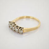 Zarter Goldring mit fünf klaren Edelsteinen auf reflektierendem Hintergrund