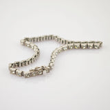 Zartes Silberarmband mit quadratischen Fassungen und funkelnden klaren Edelsteinen auf reflektierendem weißen Untergrund.