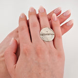 Zwei Hände mit gepflegten Nägeln und Silberring mit strukturierter, runder Fläche am Ringfinger.