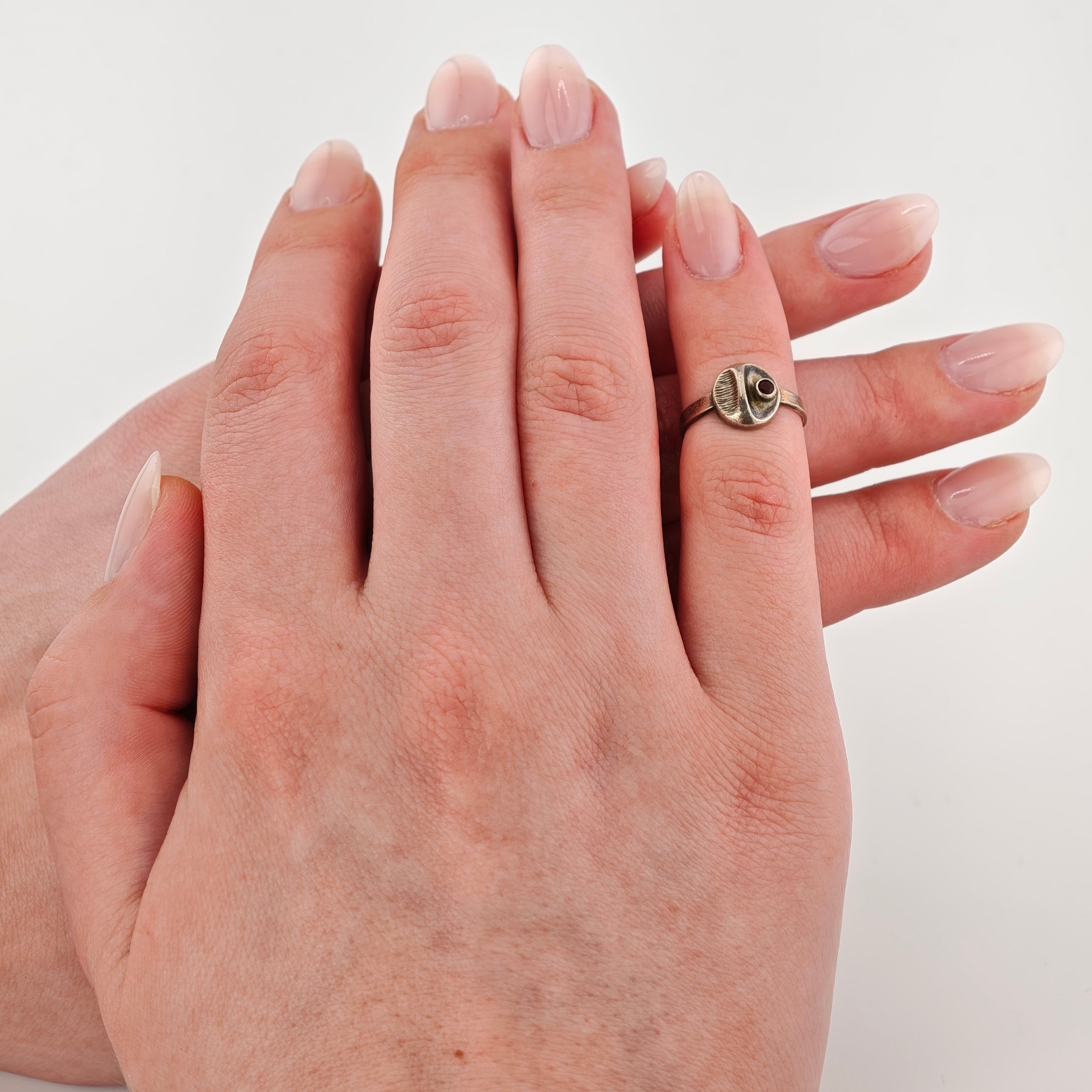 Zwei Hände sanft berührend, einer mit rundem Kunst-Ring und dunklem Detail, natürlich polierte Nägel.