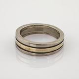 Zweiseitiger Metallring mit silbernem Außenband und goldenem Innenband auf reflektierender Oberfläche