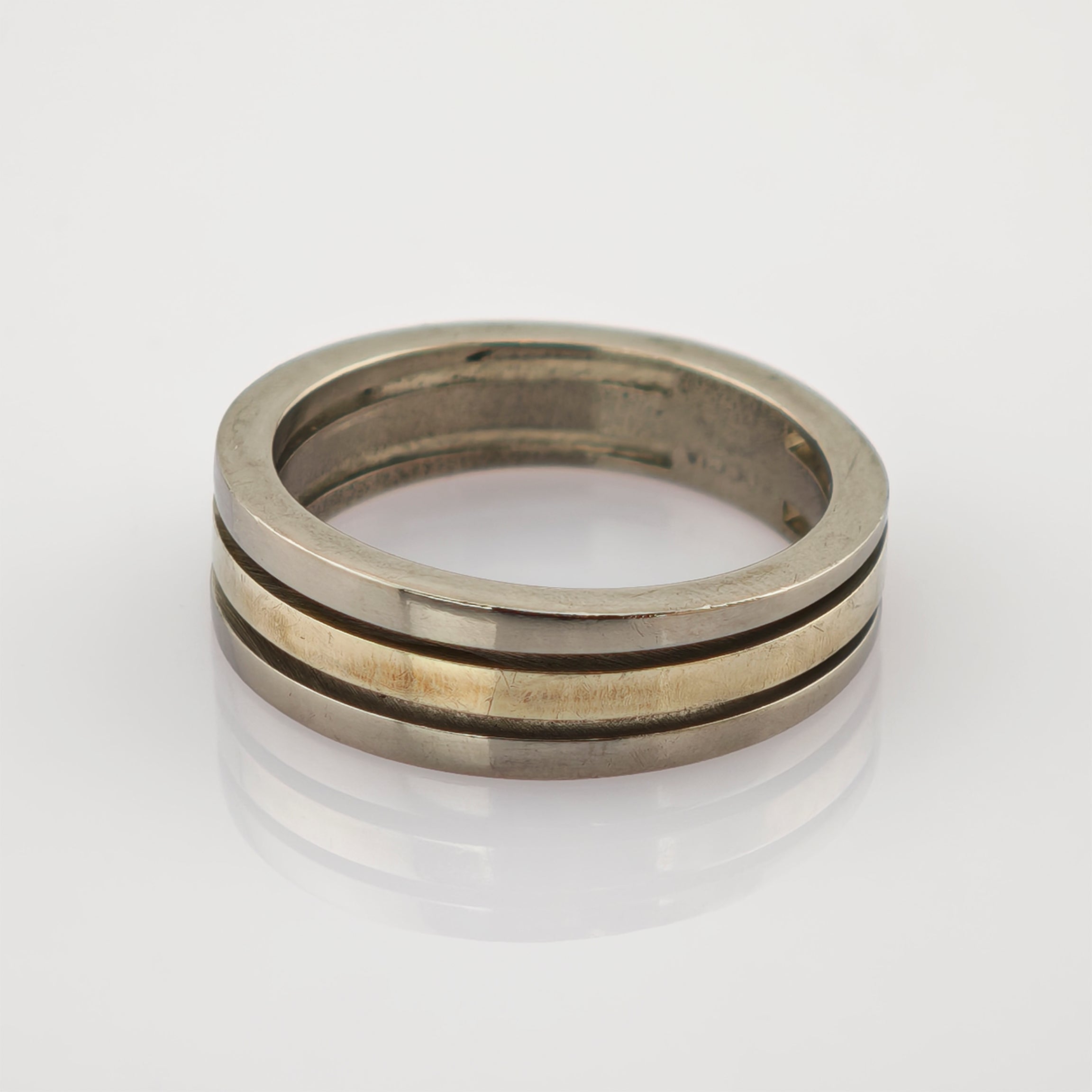 Zweiseitiger Metallring mit silbernem Außenband und goldenem Innenband auf reflektierender Oberfläche