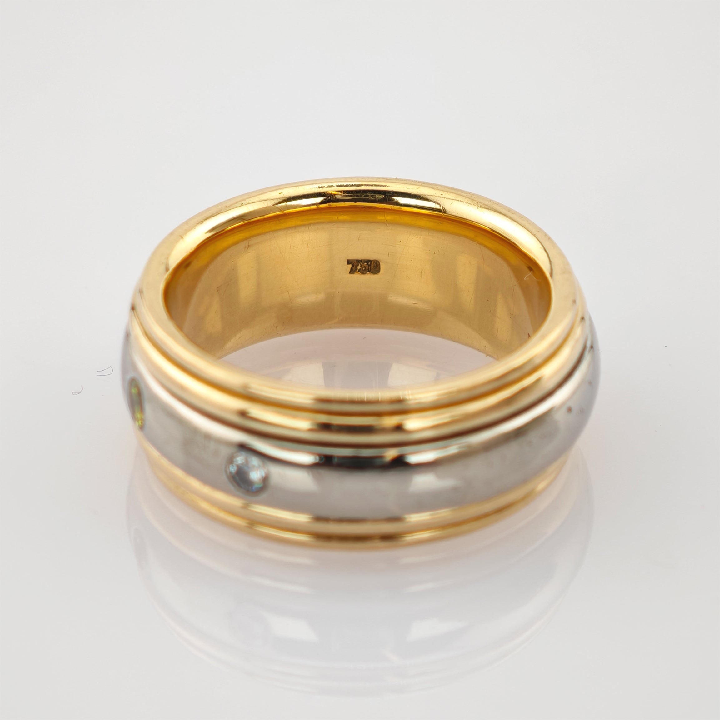 Zweisilberner Ring mit goldenem Innenring und zwei kleinen runden klaren Edelsteinen auf weißem Hintergrund